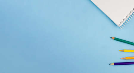 White notepad with colored pencils on a blue background. Place for your text. Education concept. View from above.の写真素材