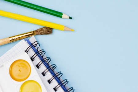 Notebook with colored pencils and paint on a blue background. Place for your text. View from above. Education concept.の写真素材