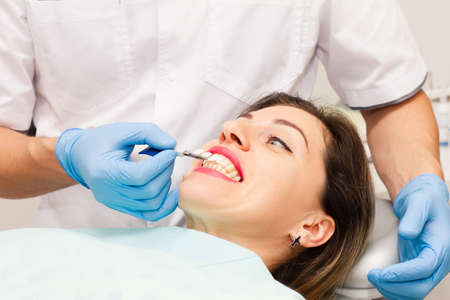 The face of a beautiful dark-haired woman with red lipstick and an open mouth. Doctor's appointment with blue gloves. Health concept.の写真素材