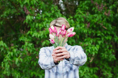 guy in a blue checkered shirt holds a bouquet of pink tulips holding them in front of him, close his face, outdoors.の写真素材