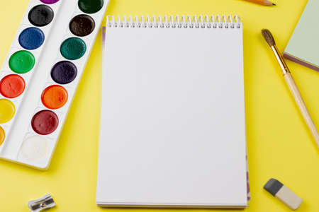 Blank notebook with colored paint and other supplies on a yellow background. View from above. Place for your text.の写真素材