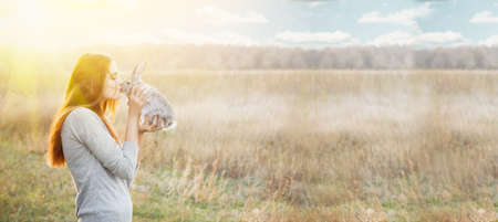 a young woman with red hair and a gray sweater. Caucasian appearance holds a small gray fluffy domestic rabbit, and smiles at him cutely, photo baner, concept for the spring holidaysの写真素材