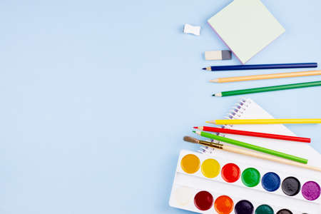 Notebook with paints and crayons on a blue background. Place for your text. View from above. Education concept.の写真素材
