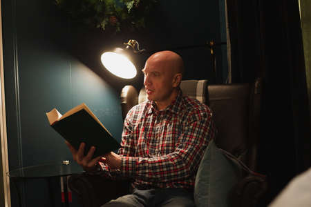 A handsome, charming man, dressed in a plaid shirt and jeans, holds a book in his hands and reads it in surprise.の写真素材