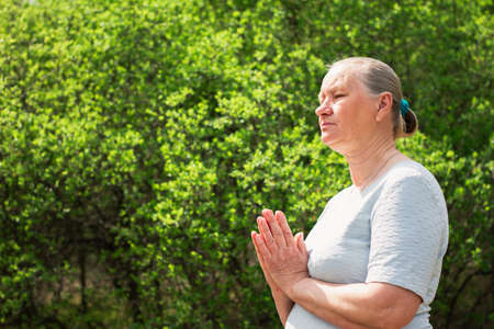 A calm elderly woman, dressed in white clothes, meditates in nature. Practice yoga, relieve stress or renew energy. Healthy lifestyle concept.の写真素材