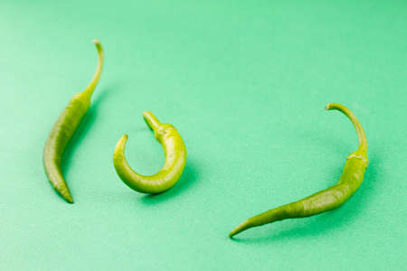 three small capsicum green hot chili peppers on a pastel green background, top view close-up. Food background, vegetarian cuisine conceptの写真素材