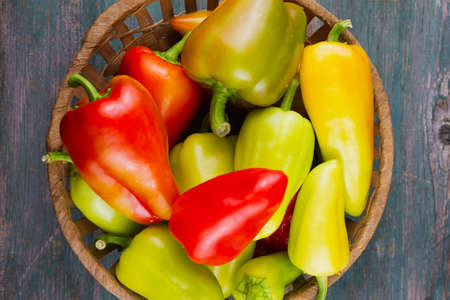 ripe multi-colored bell peppers in a wicker basket on an old wooden background, the concept of ripe vegetables, close upの写真素材