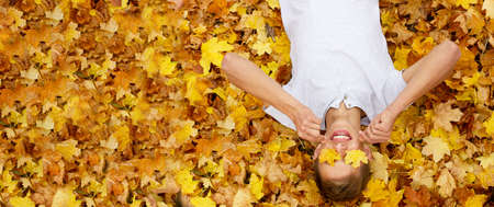 young handsome guy of Caucasian ethnicity in a white T-shirt lies on autumn yellow maple leaves and closes his eyes with leaves with his hands, copy space, photo banner. Concept for autumn discountsの写真素材