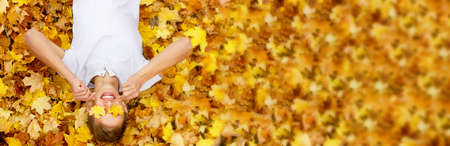 young handsome guy of Caucasian ethnicity in a white T-shirt lies on autumn yellow maple leaves and closes his eyes with leaves with his hands, copy space, photo banner. Concept for autumn discountsの写真素材