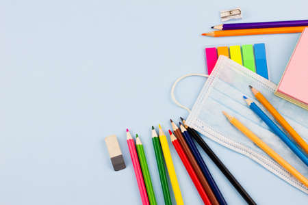 Various school supplies with a mask in the corner on a blue background. Education concept. Place for text. View from above.の写真素材