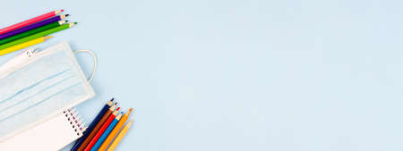 Multicolored stationery with a mask on a blue pastel background. Education concept. View from above. Place for text. Photo banner. Epidemic.の写真素材