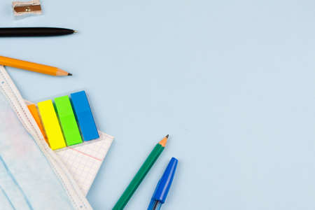 School supplies with a mask on a blue background. View from above. Place for text. Epidemic. Education concept.の写真素材
