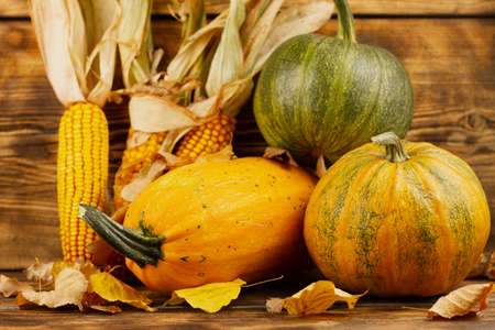 Yellow and green pumpkins with corn on a wooden background. Autumn harvest concept. Autumn still life.の写真素材