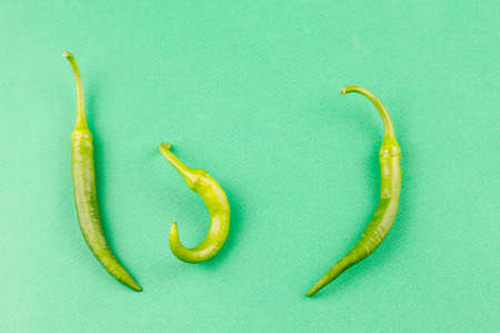 three small capsicum green hot chili peppers on a pastel green background, top view close-up. Food background, vegetarian cuisine conceptの写真素材