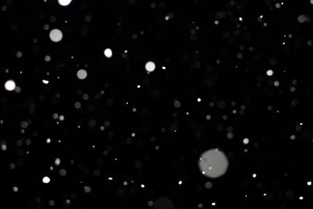 Freeze motion of white powder coming down, isolated on black, dark background. Abstract design of falling dust cloud. Particles cloud screen saver, wallpaper with copy space. Rain, snow fall conceptの写真素材