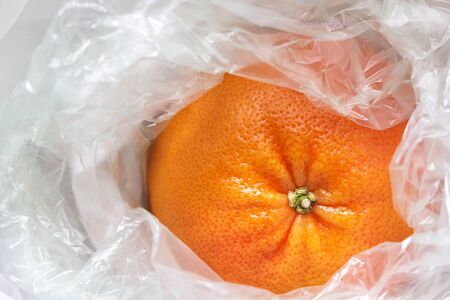 Closeup of a grapefruit wrapped in a white plastic bag. Single use plastic, pollution problem, zero waste, ban plastic concept.の写真素材