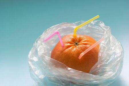 Grapefruit with plastic straws in a plastic bag on blue background. Ban plastic, zero waste concept....