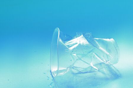 Crumpled plastic glass with water drops on blue background. Zero waste, recycling, pollution...
