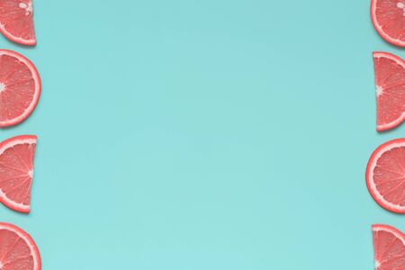 A frame of pink citrus slices on bright blue background. Summer fruit minimalism. Flatlay, top view,...