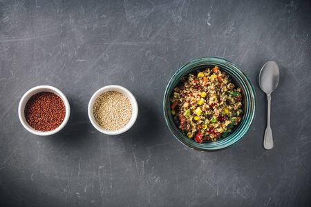 Quinoa salad bowl with colorful vegetables: green beans, carrot, corn, bell pepper, peas and two cups with red and white quinoa seeds. Healthy diet, vegetarian food concept. Top view, flat lay, copy space.の写真素材