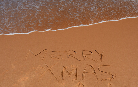 Merry Xmas written on sand at sunset. Merry Christmas lettering on the beach. "Merry Xmas" drawn on sand on a beach, closeup shot. Merry Christmas  written in sand, on tropical beach.の写真素材