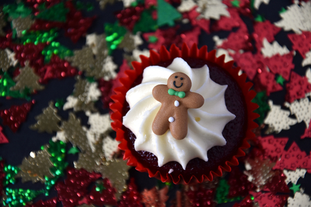 Christmas cupcake with Gingerbread Man and whipped cream topping. Xmas festive holiday food dessert. Christmas concept muffin with decoration and Christmas tree confetti background, selective focus.の写真素材
