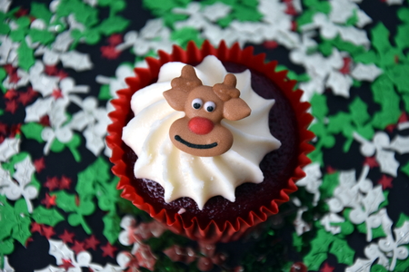 Christmas cupcake with Reindeer face and whipped cream topping. Xmas festive holiday food dessert. Christmas concept muffin with decoration on top, Christmas tree confetti background, selective focus.の写真素材