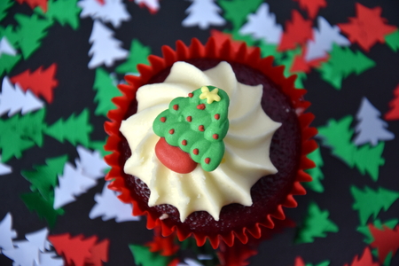 Christmas cupcake with Santa face and whipped cream topping. Xmas festive holiday food dessert. Christmas concept muffin with decoration on top and Christmas tree confetti background, selective focus.の写真素材