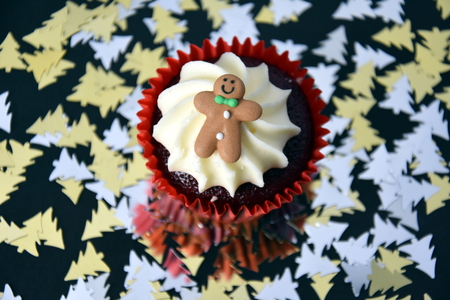 Christmas cupcake with Gingerbread Man and whipped cream topping. Xmas festive holiday food dessert. Christmas concept muffin with decoration, Christmas tree confetti background, selective focus.の写真素材