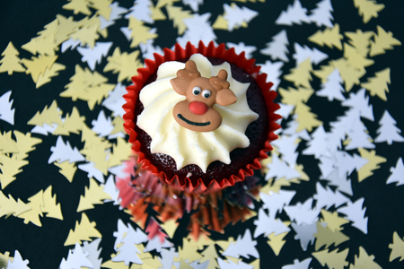 Christmas cupcake with Reindeer face and whipped cream topping. Xmas festive holiday food dessert. Christmas concept muffin with decoration on top, golden stars confetti background, selective focus.の写真素材