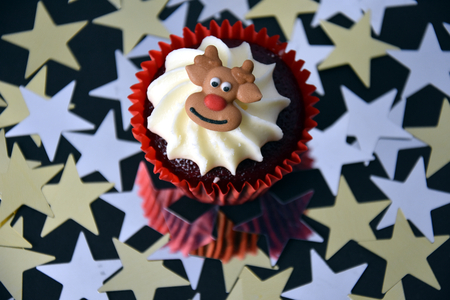 Christmas cupcake with Reindeer face and whipped cream topping. Xmas festive holiday food dessert. Christmas concept muffin with decoration on top, golden stars confetti background, selective focus.の写真素材