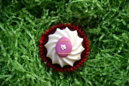 Easter home made muffins decorated with easter egg. Easter concept, pink egg on top of the red and white cupcake in green nest.の写真素材
