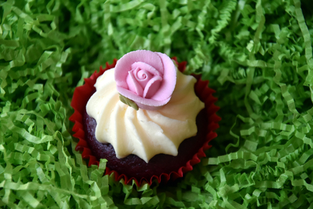 Muffins decorated with rose flower on green background. Spring, Mother's Day, Valentine's Day concept. Homemade cupcake with whipped cream and pink rose spring flower on green grass background.の写真素材