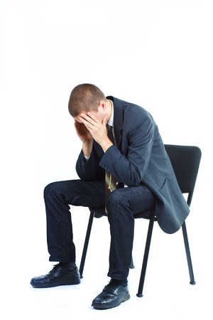 Businessman sitting on a chair with head between hands, looking down - isolated on whiteの写真素材