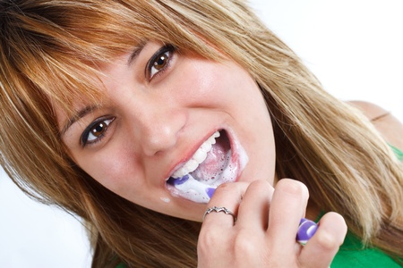 Close-up of a young woman with blond hair, brushing her teeth with foaming toothpaste - isolated on whiteの写真素材