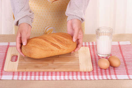 Woman hands laying the bread at the table, milk and eggs