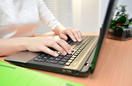 Closeup of business woman's hand typing on computer keyboard with green folderの写真素材