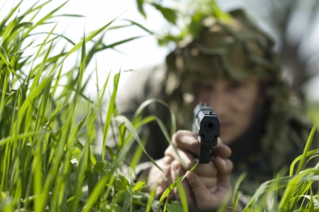 Military Camouflaged man in forest with black handgun. Focus on gunpoint