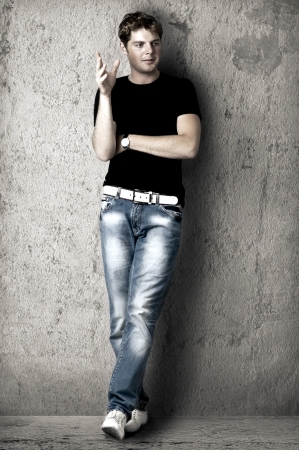 Young handsome sexy man in black t-shirt and blue jeans is leaning against the wallの写真素材