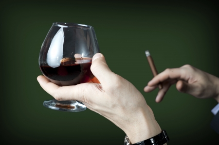 Old brandy in glass and cigar in male hand on green backgroundの写真素材