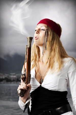 Girl pirate blows a smoke from a trunk of a old pistol の写真素材