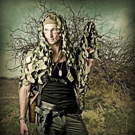 Military Camouflaged man in forest with automatic and hand gunの写真素材