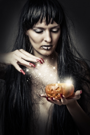 Sexy brunette woman witch making magic to pumpkinの写真素材