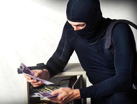 Professional burglar in black ski mask  opened a small safe, holding a lot of moneyの写真素材
