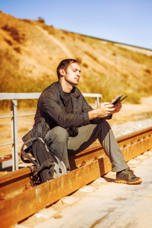 bright picture of travelling young man with backpack. He sitting on railroad and writes on a Tablet PCの写真素材