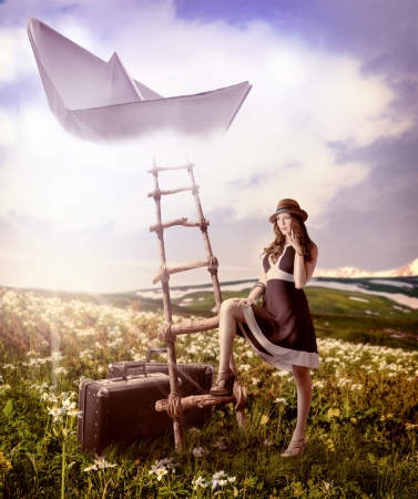 dreaming about travel Beautiful woman with suitcases standing near the ladder to the flying paper boat in the cloudsの写真素材