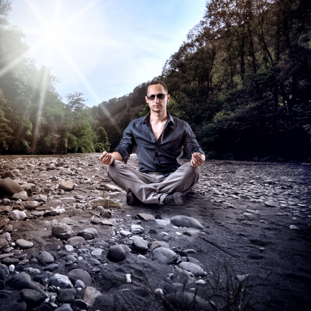 Young fashion man in dark blue shirt and gray pants sitting on sand with stones outdoorの写真素材
