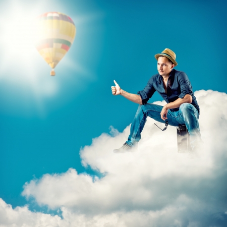 Young handsome man traveller sitting on a clouds with a sign hitch hikingの写真素材