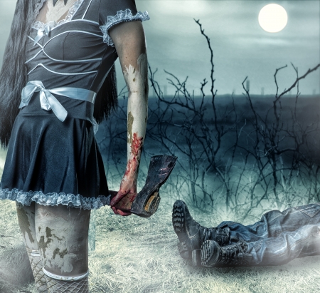 Halloween horror concept. Woman zombie holding axe in hands. In the background lies the  legs of corpse manの写真素材