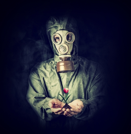 Concept. Hope after environmental protection. Man in gas mask holding tulip flower in palmsの写真素材